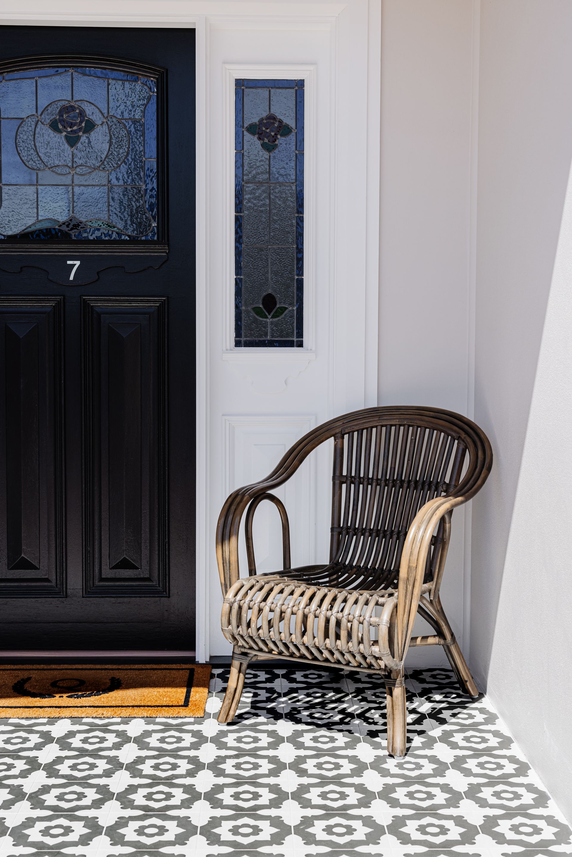 Wicker chair on a patterned porch, beside a black door with frosted glass.
