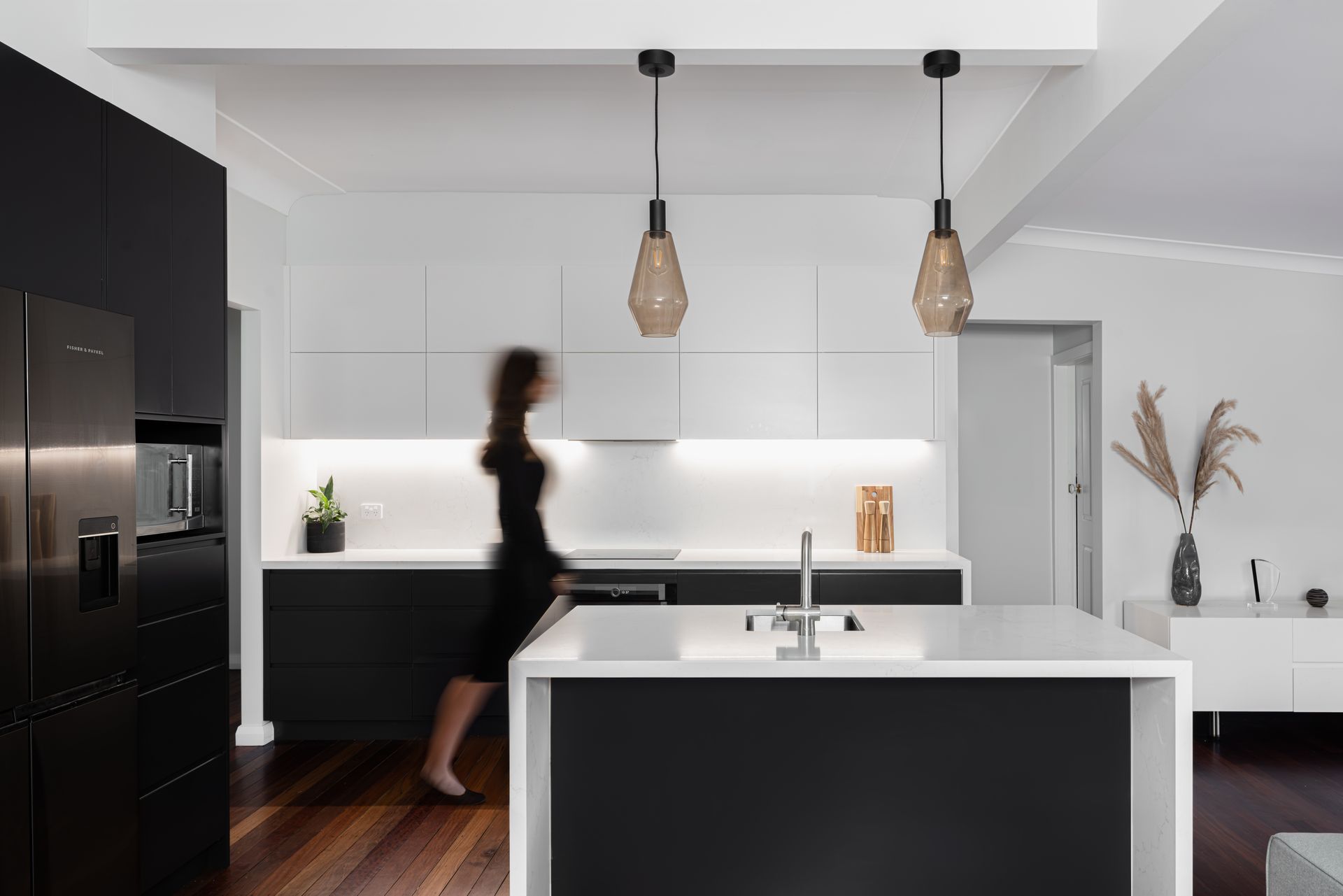 Modern kitchen with black and white cabinets, island, and a woman walking past.