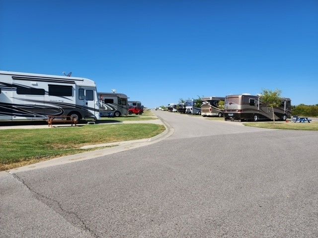 RV park with paved road, RVs parked on grass, blue sky.