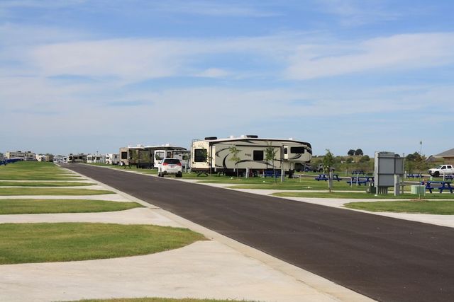 RV park with paved road, RVs, picnic tables, and blue sky.