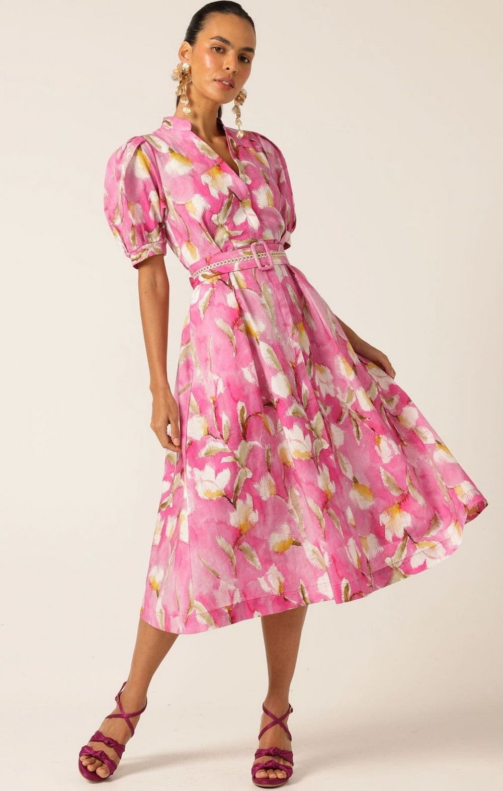 Woman in a pink floral dress with puff sleeves and heels, posing against a white backdrop.