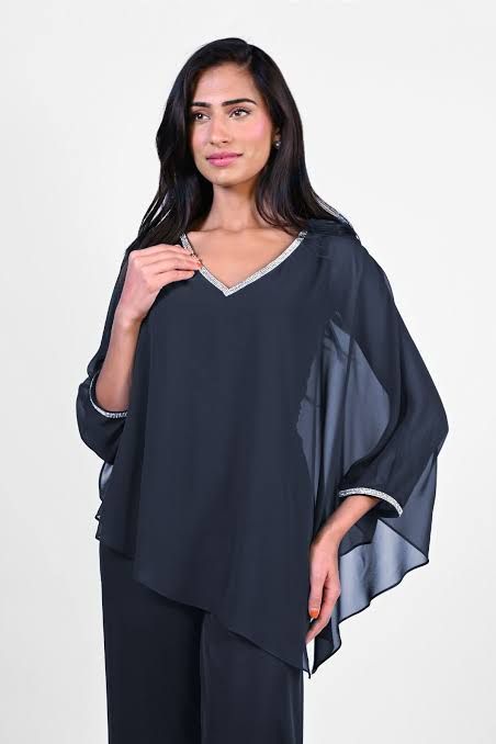 Woman wearing a blue dress with cape sleeves, posing with a smile. She's standing indoors with a white background.