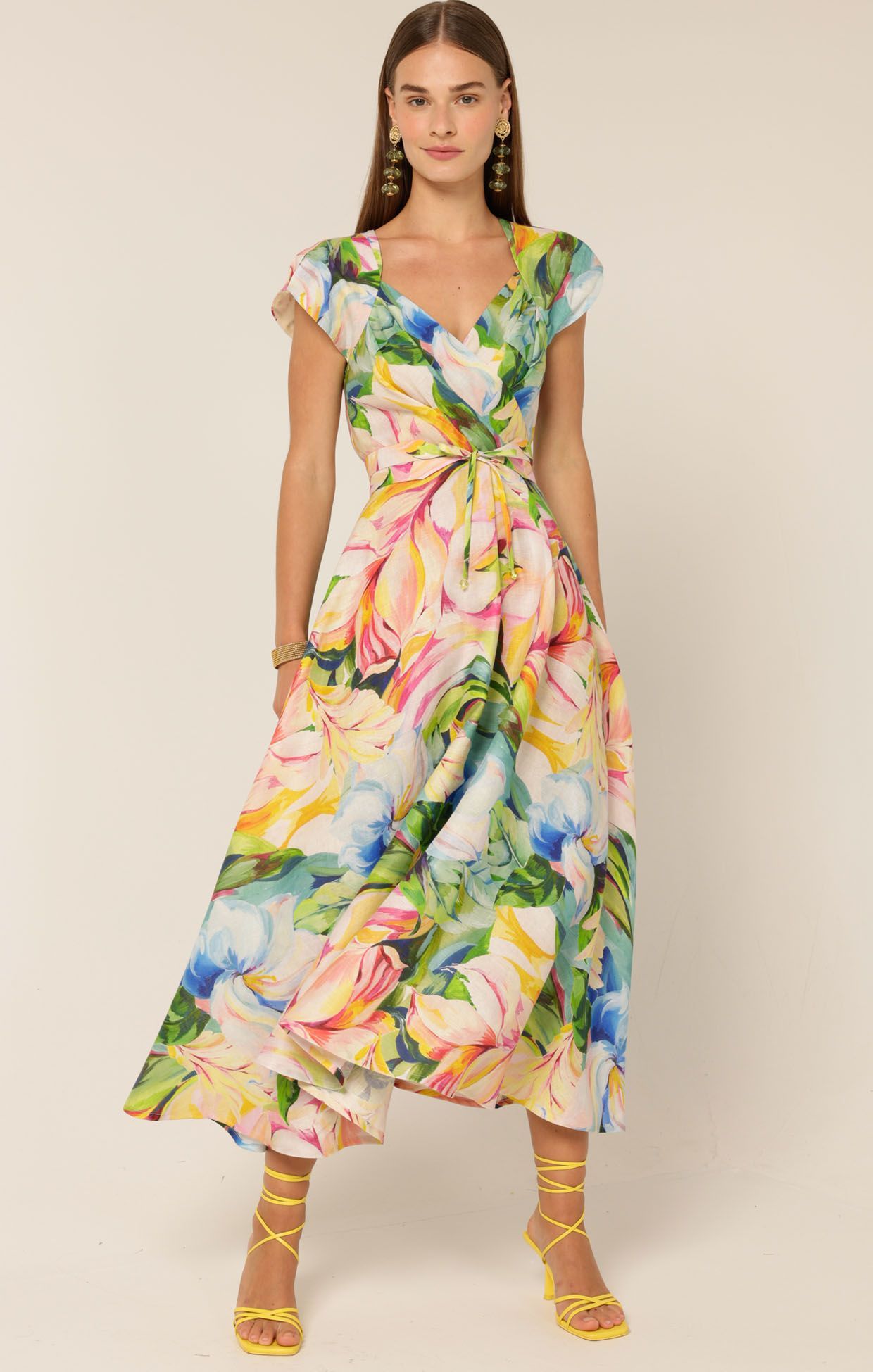 Woman wearing a floral print midi dress, cinched at the waist, with yellow heels, posing.