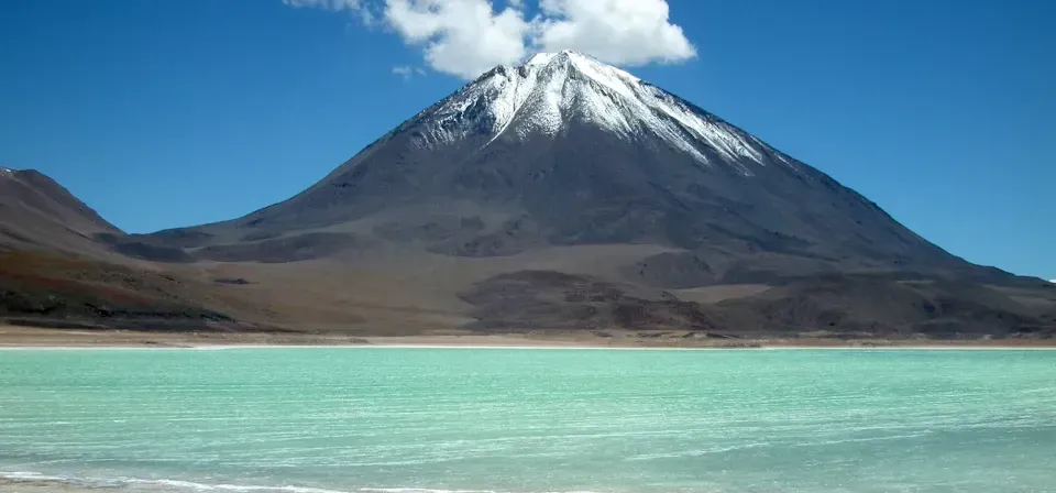 Montaña nevada sobre un lago turquesa bajo un cielo azul despejado