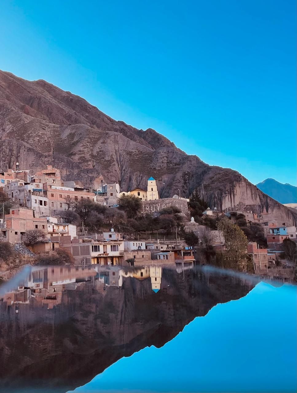 Pueblo de montaña reflejado en un lago azul en calma al anochecer