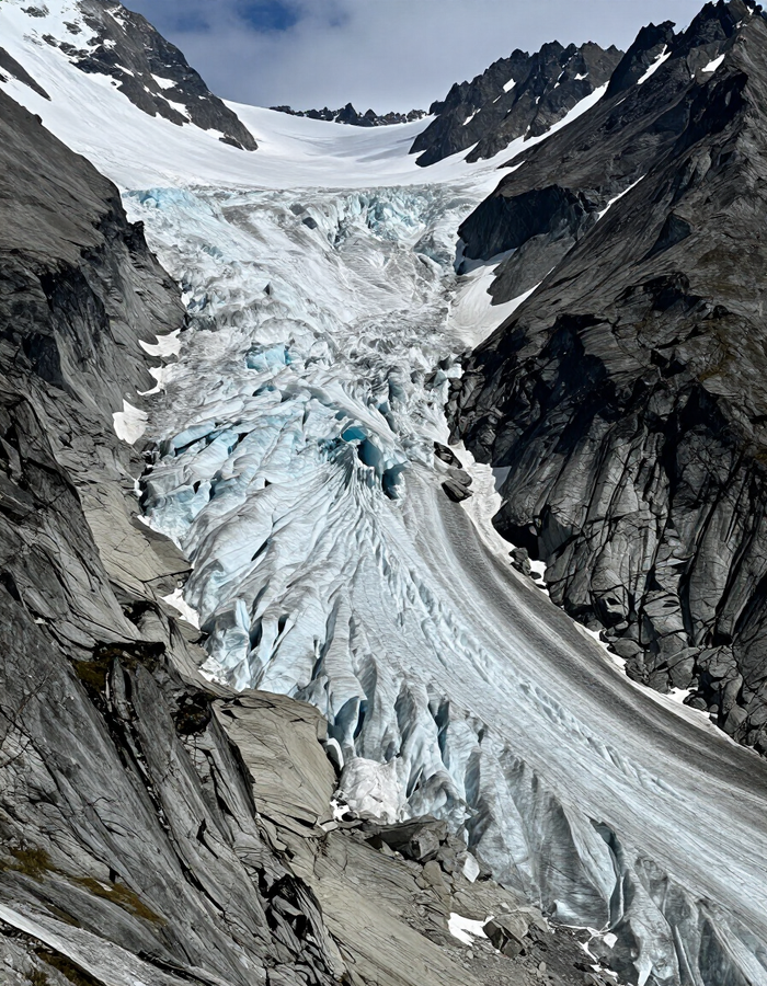 Un glaciar de montaña empinado que fluye entre acantilados rocosos, con manchas de nieve en lo alto