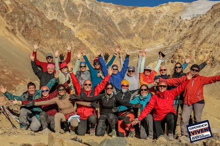 Cinco excursionistas con mochilas subiendo por una empinada ladera rocosa, con picos escarpados al fondo