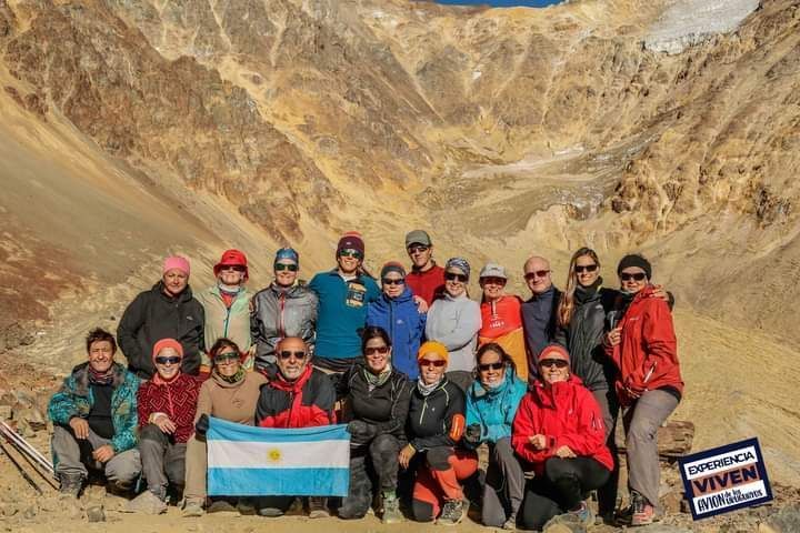 Grupo de excursionistas posando en un paisaje montañoso rocoso, con una bandera argentina en las manos.