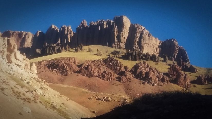 Cresta rocosa de montaña en el desierto bajo un cielo azul despejado, con laderas ocres y rojizas en primer plano