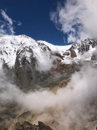 Cumbres montañosas cubiertas de nieve bajo un cielo nublado, con niebla deslizándose por las laderas