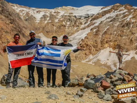 Cuatro excursionistas sosteniendo las banderas de Ecuador y Grecia en un valle montañoso nevado