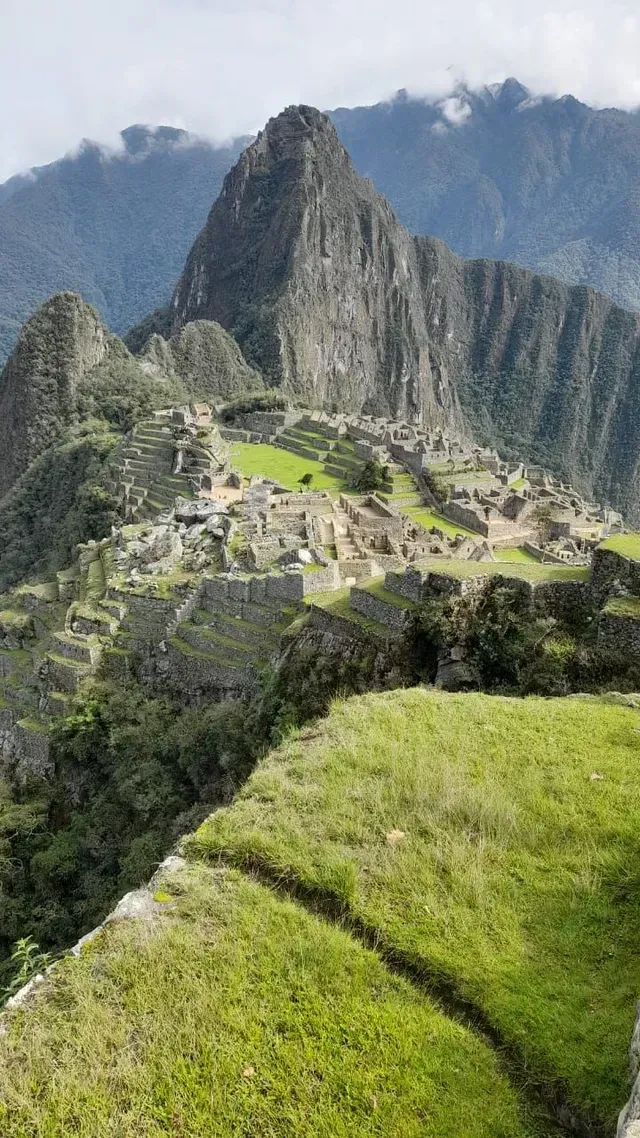 Ruinas de Machu Picchu al pie de escarpadas montañas verdes y un pico envuelto en niebla