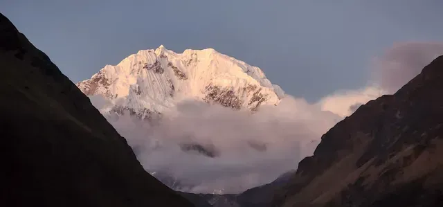 Montaña nevada que resplandece al amanecer entre las oscuras laderas del valle y las nubes bajas