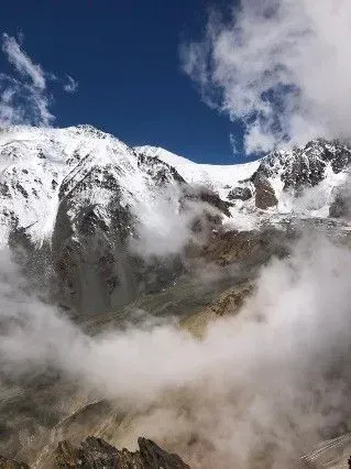 Cumbres montañosas cubiertas de nieve sobre las nubes, bajo un cielo azul