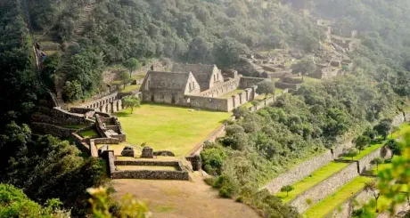 Ruinas de piedra y muros aterrazados alrededor de un patio cubierto de hierba, en un valle montañoso boscoso