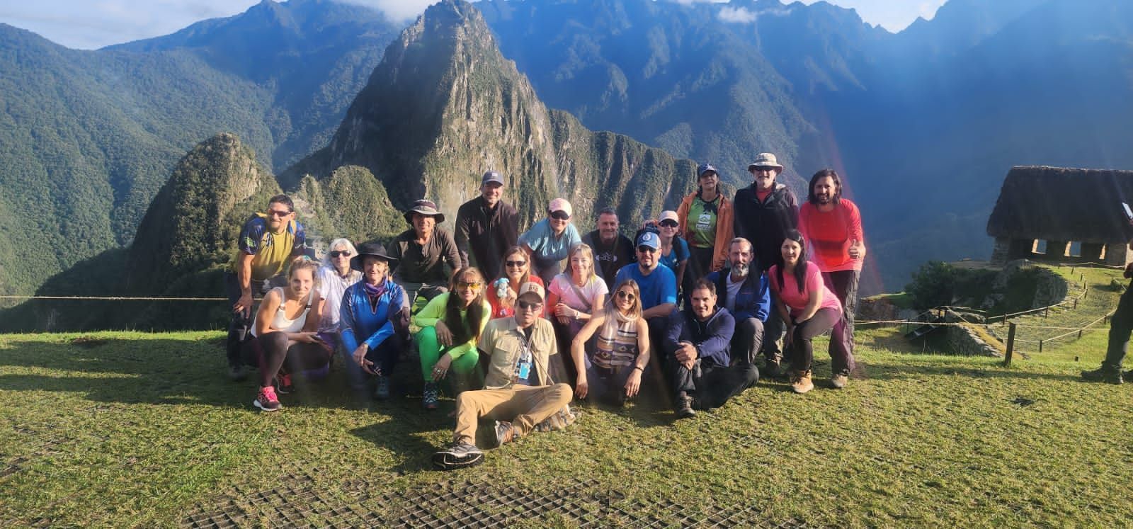 Grupo de excursionistas posando en un mirador cubierto de hierba, con imponentes cumbres al fondo
