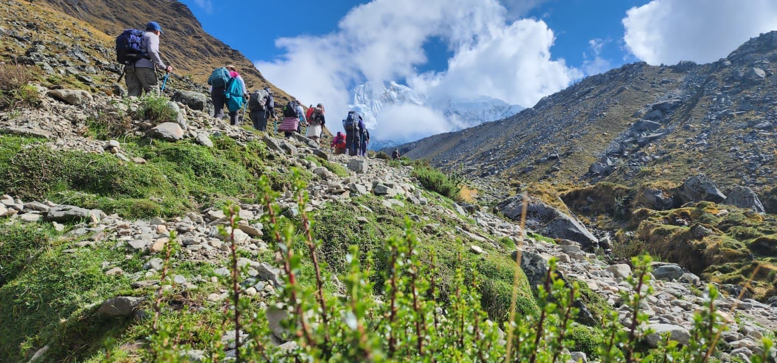 Excursionistas subiendo por un sendero rocoso de montaña bajo un cielo azul con nubes