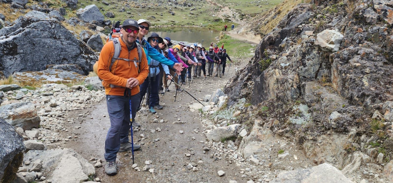 Excursionistas con mochilas recorren un sendero rocoso de montaña con el cielo nublado