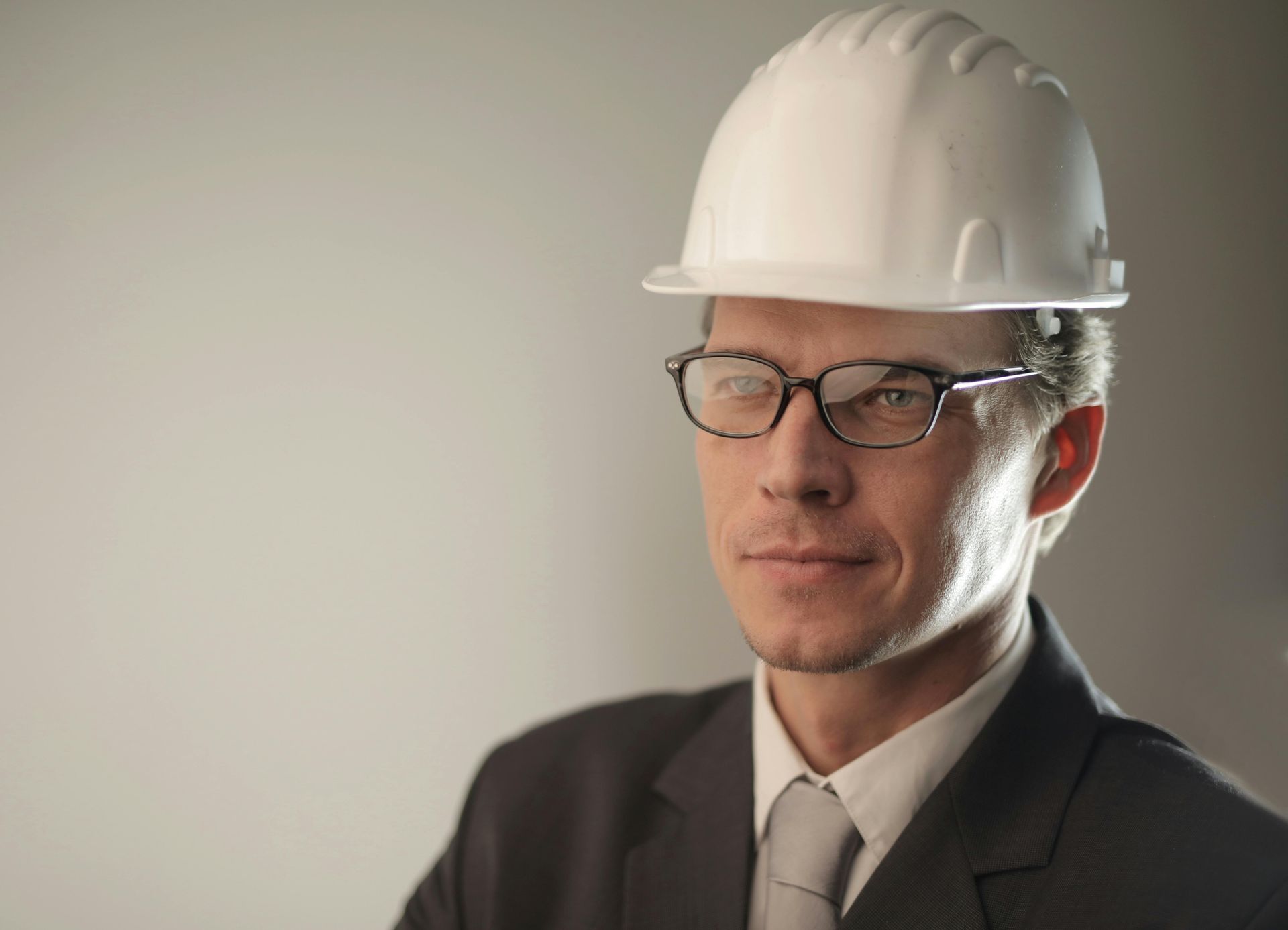 Professional in a white hard hat and glasses, wearing a dark suit, against a plain background.