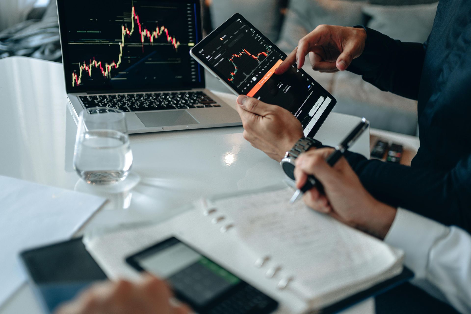 Two people reviewing stock charts on a laptop and smartphone at a desk