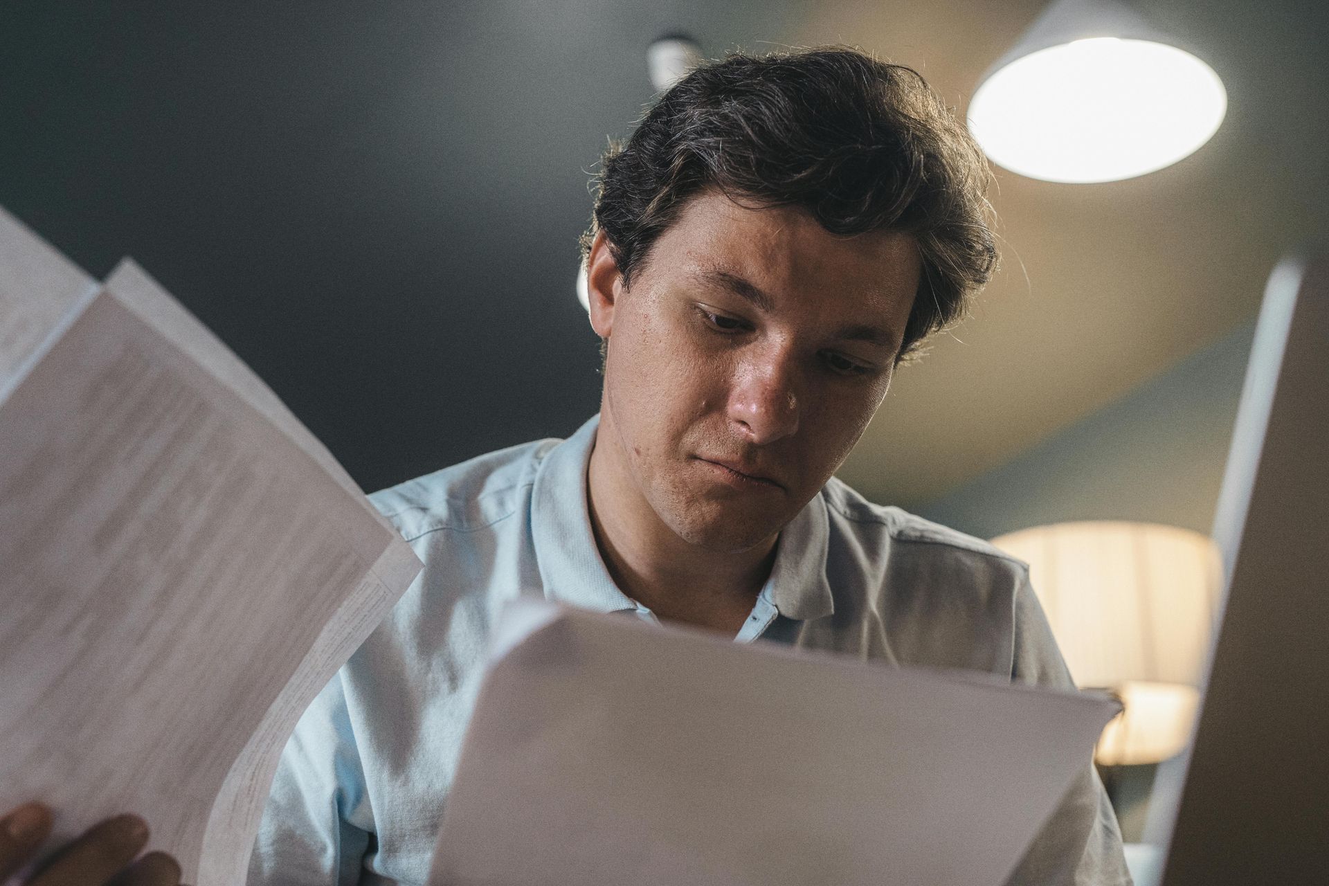 Man in a navy suit reviewing papers at a glass table in a dimly lit office