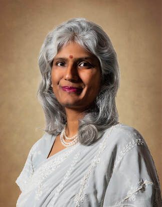 Woman with gray hair and a pearl necklace smiling in a light-colored blouse.