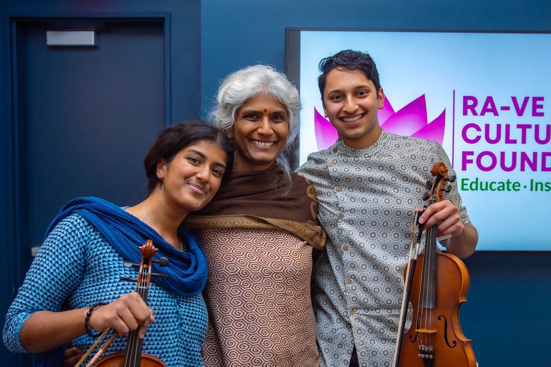 Three people smile, holding violins. Backdrop is a logo for a cultural foundation.