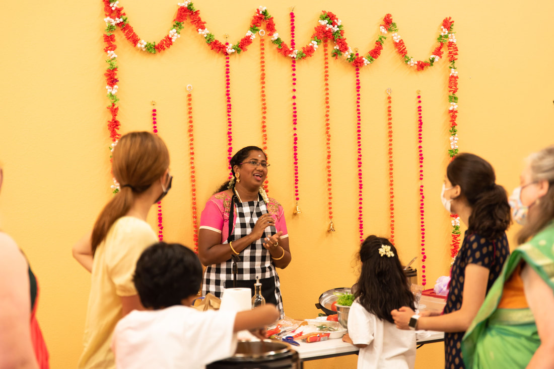 Woman in a kitchen talking to a small group with decorated wall behind them.