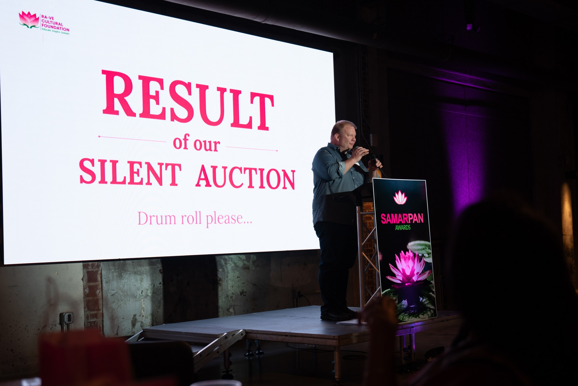 Man speaking at a silent auction; screen displays