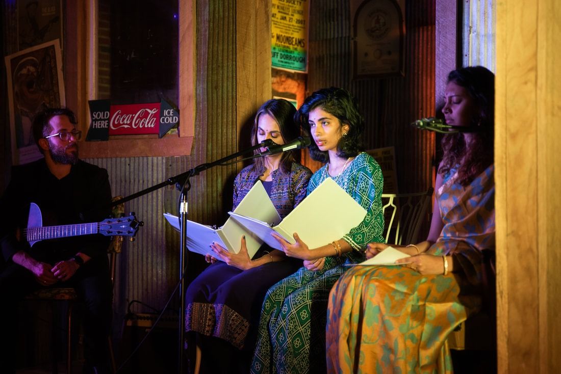 Musicians performing: guitarist, three women singing from sheet music, warm lighting.