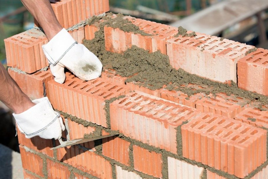 Gloved worker laying mortar between orange bricks on a wall under construction