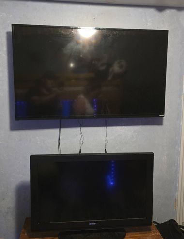 Two flat-screen TVs mounted one above the other on a gray wall, both turned off.