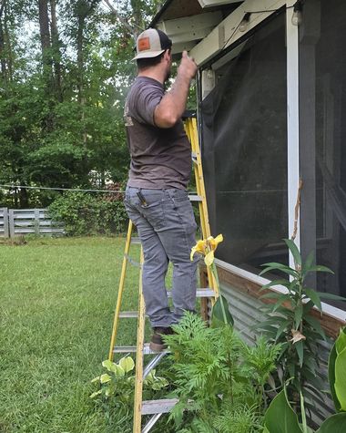 Person on a yellow ladder repairing the exterior of a house beside a screened porch.