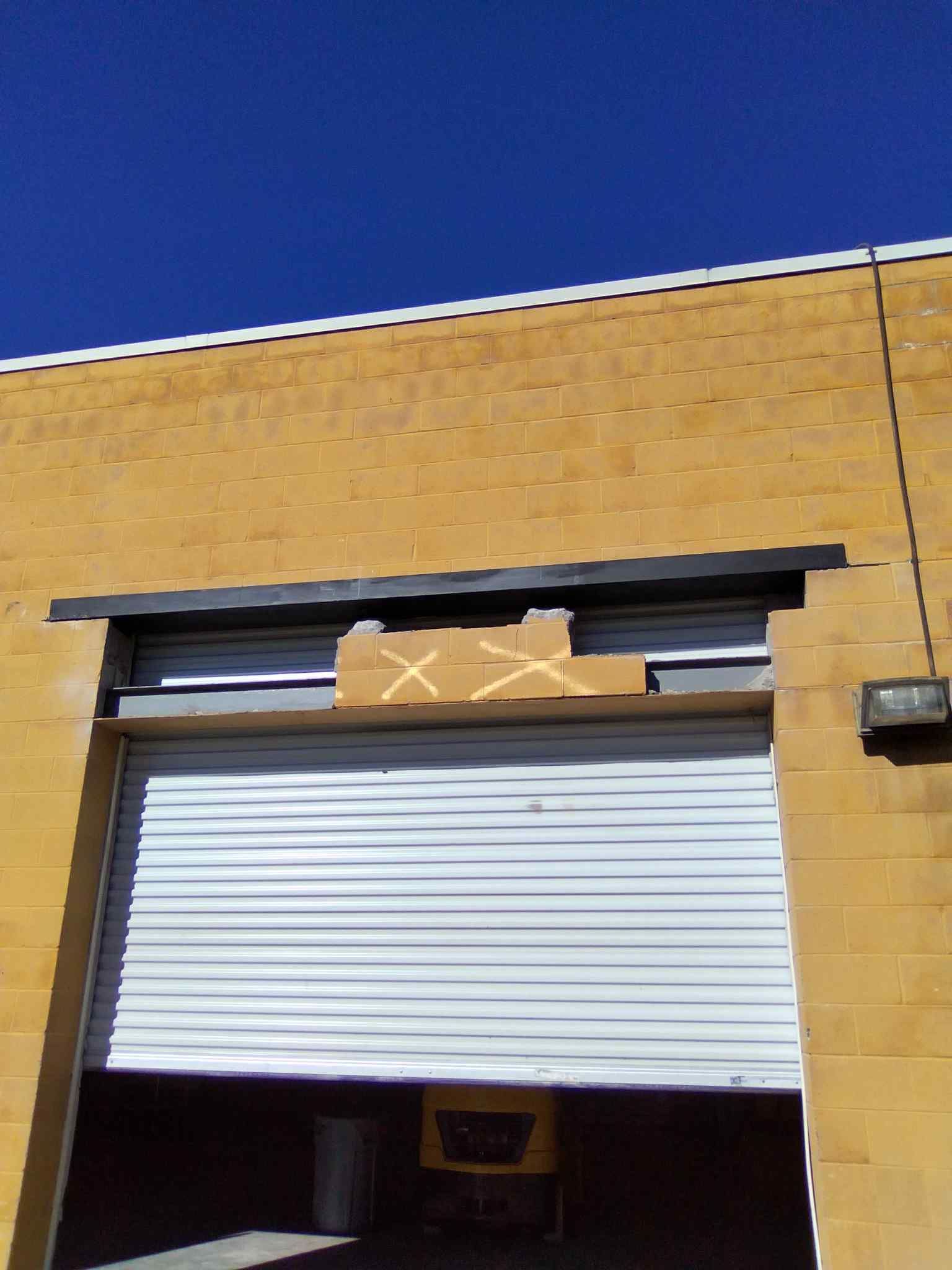 Brick building with a partially open white roll-up door and boxes visible above the entrance.