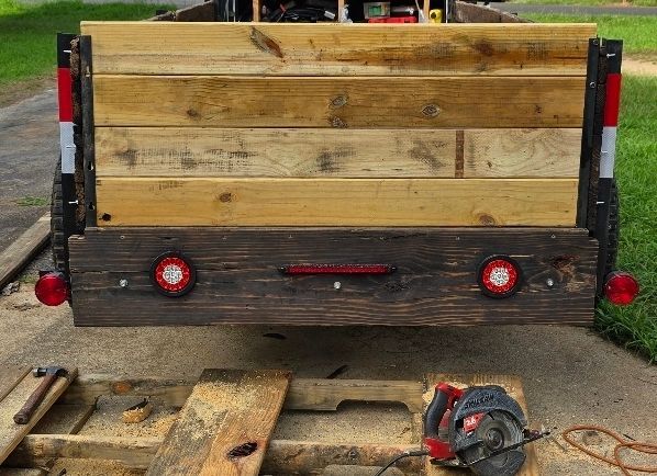 Wooden utility trailer rear with red reflectors, parked on a grassy, muddy surface.