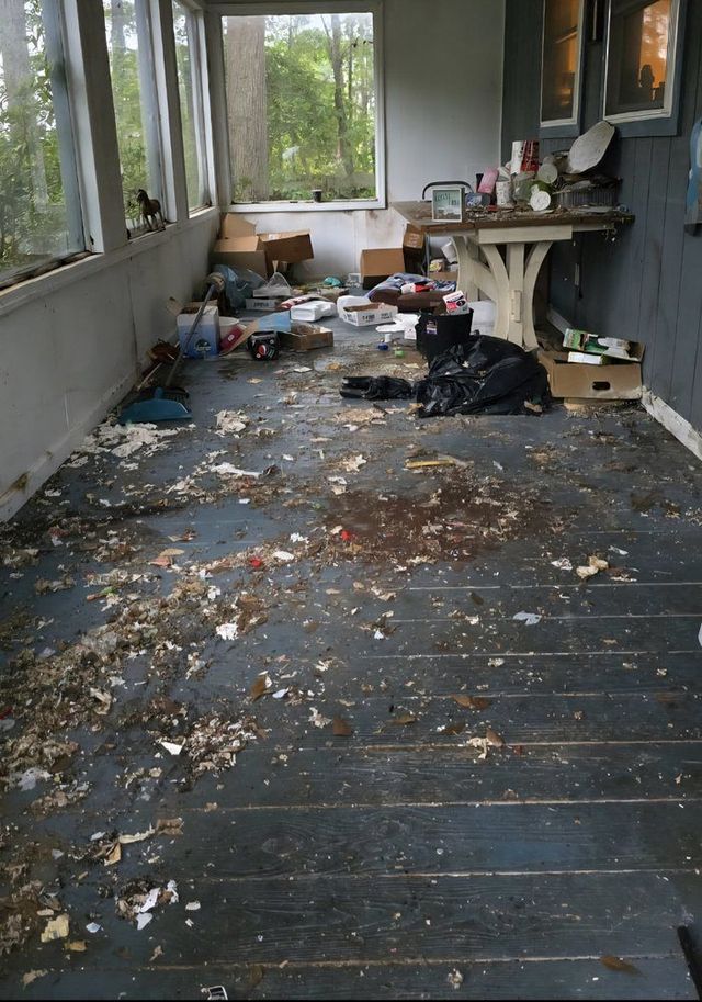 Messy porch with scattered leaves, trash, and a black bag beside a small table and windows.
