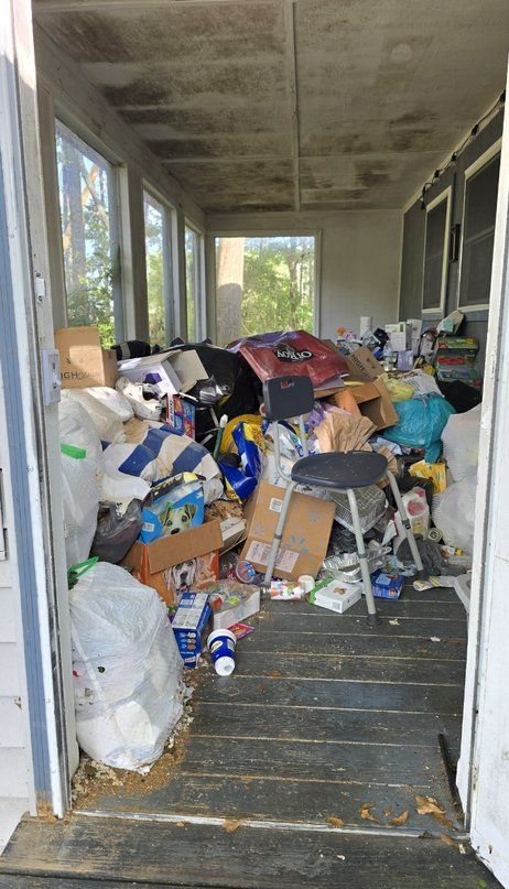 Cluttered porch filled with boxes, bags, and scattered items, with a stool in the center.