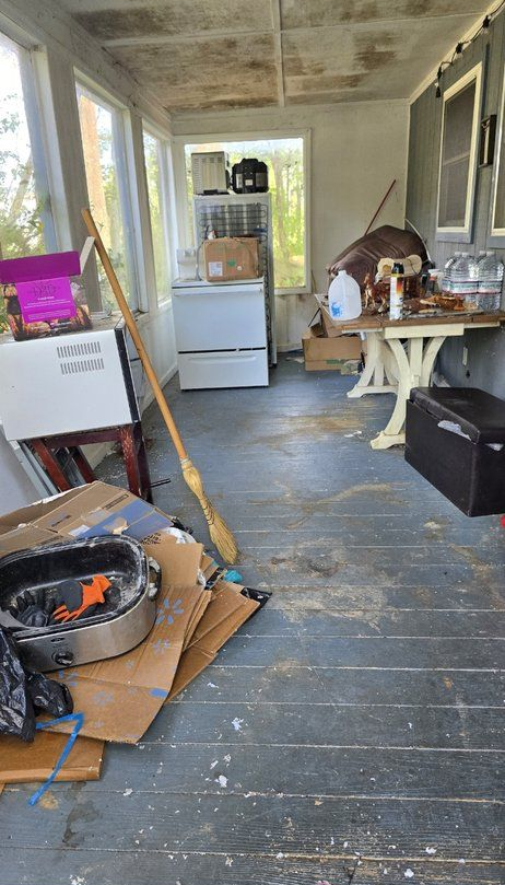 Cluttered narrow hallway with chairs, boxes, a refrigerator, and a black stove on a worn wooden floor.