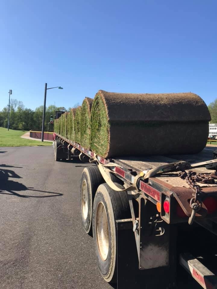 A truck is carrying rolls of grass on a trailer.