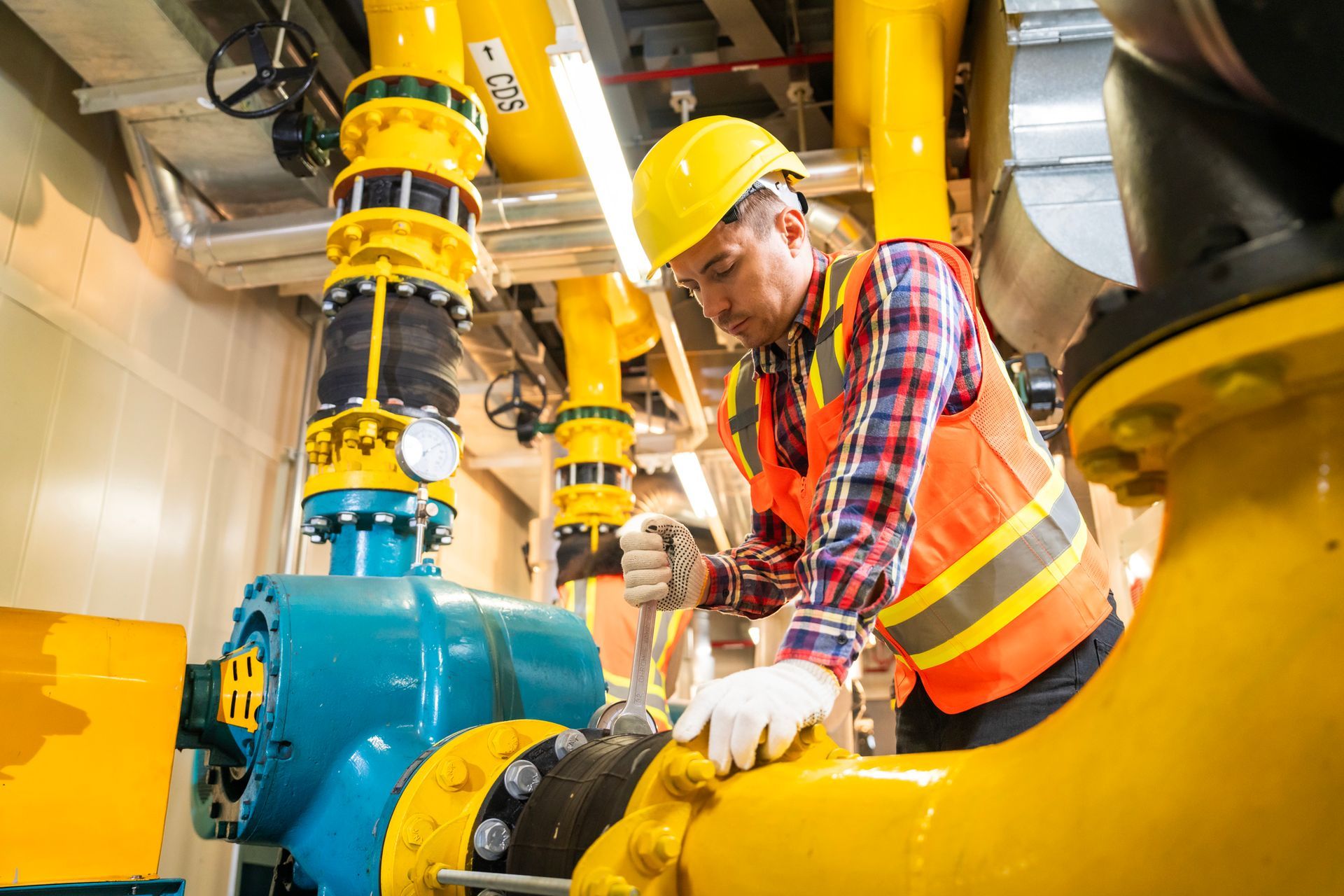 A male technician is adjusting industrial equipment with yellow pipes and pressure gauges.