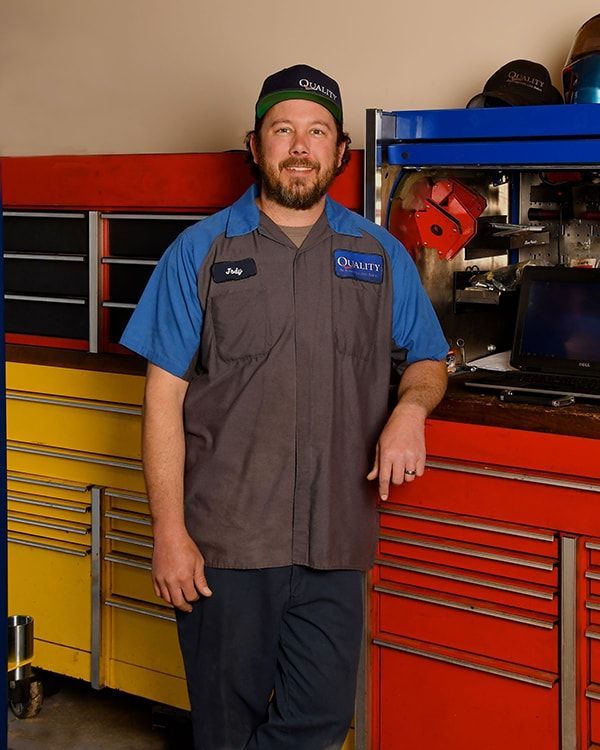 Mechanic in blue and gray work shirt standing by red tool cabinets in a garage | Quality Automotive Servicing
