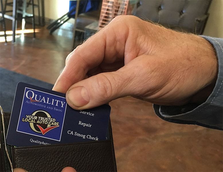 Hand holding a blue and black business card with a quality logo and contact details | Quality Automotive Servicing