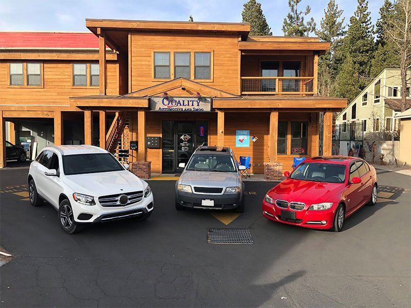 Three parked cars in front of a rustic wooden hotel or lodge entrance | Quality Automotive Servicing