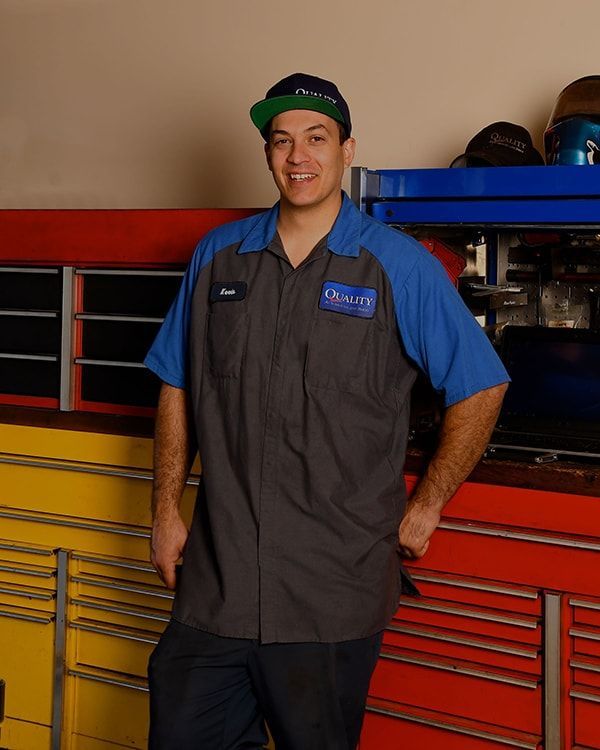 Smiling mechanic in gray vest and blue shirt standing in front of colorful tool cabinets | Quality Automotive Servicing