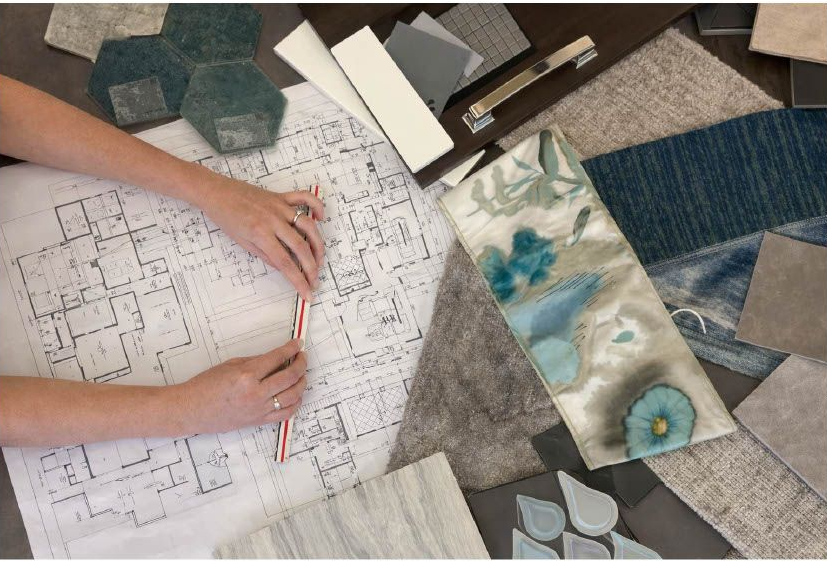 Hands drafting a quilt pattern on graph paper beside fabric swatches and sample quilt blocks