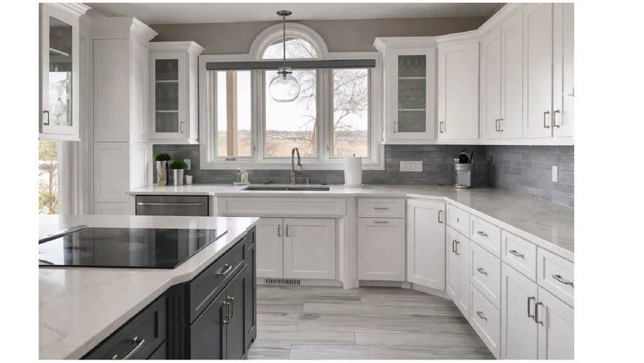 Bright white kitchen with black countertops, gray backsplash, and a large arched window over the sink
