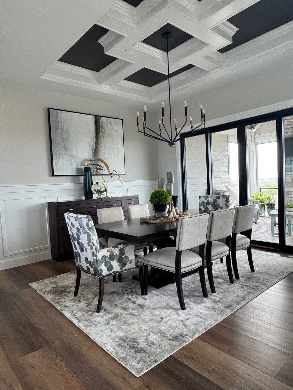 Elegant dining room with coffered ceiling, dark wood table, patterned chairs, and large windows.