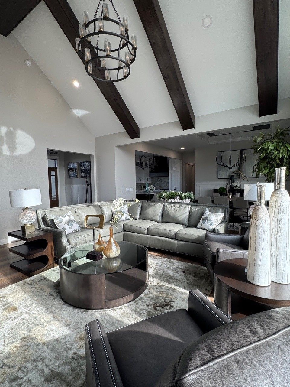 Bright living room with gray sectional, black coffee table, vaulted ceiling beams, and chandelier