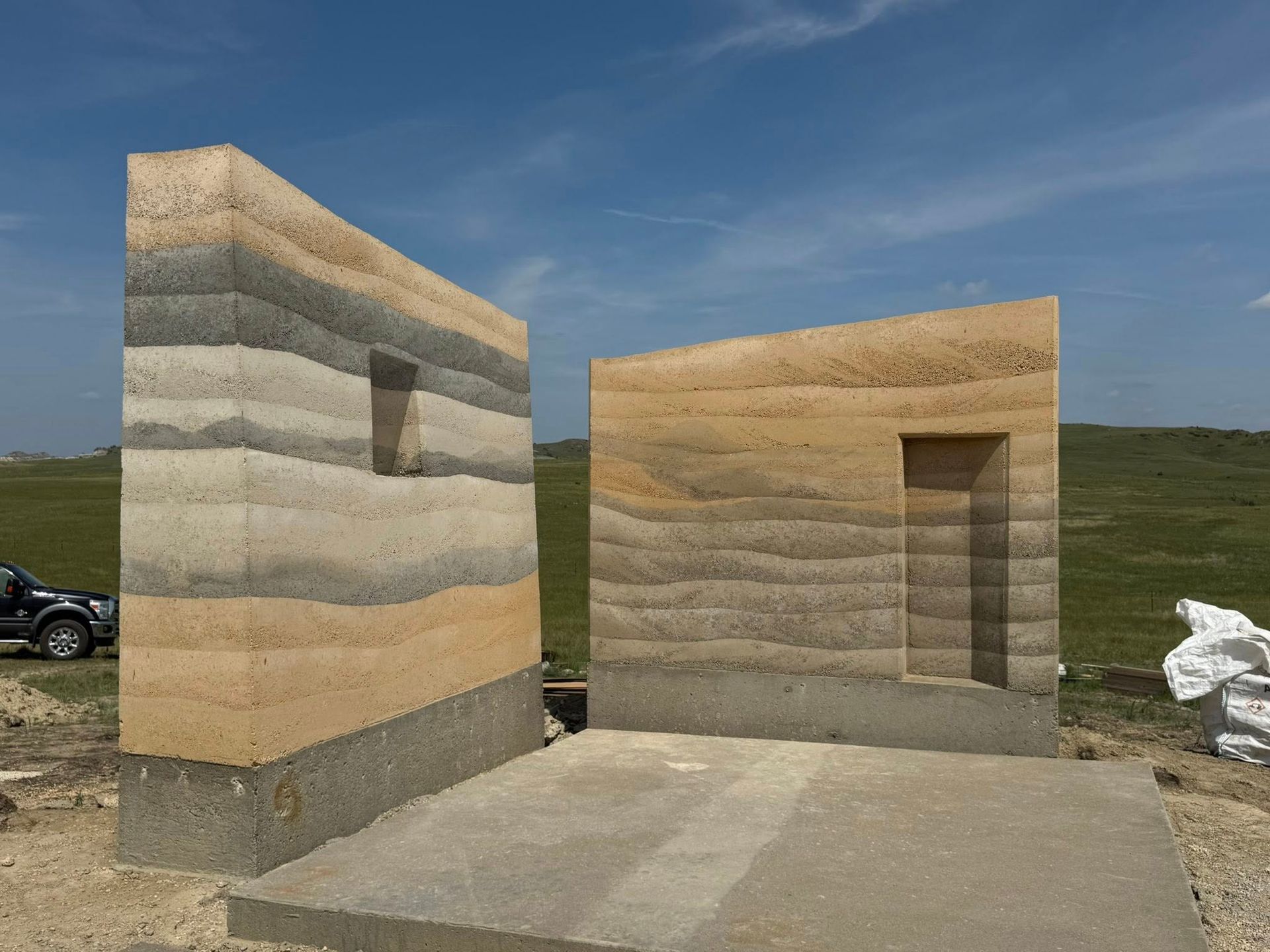 Two small stone-colored block structures in a grassy field under a blue sky