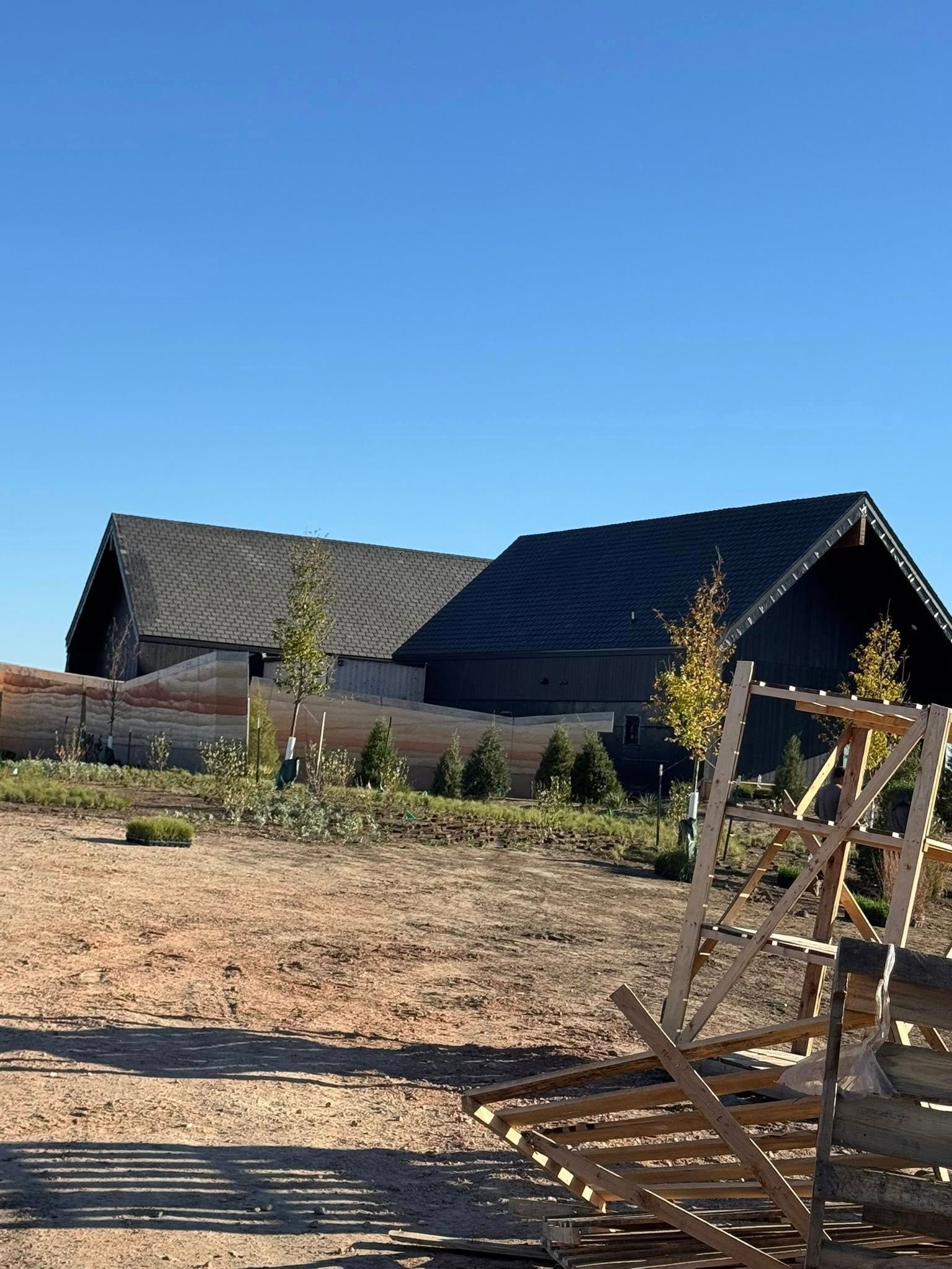 Modern house with dark roofs on a dry hillside under a clear blue sky; wooden structure in foreground